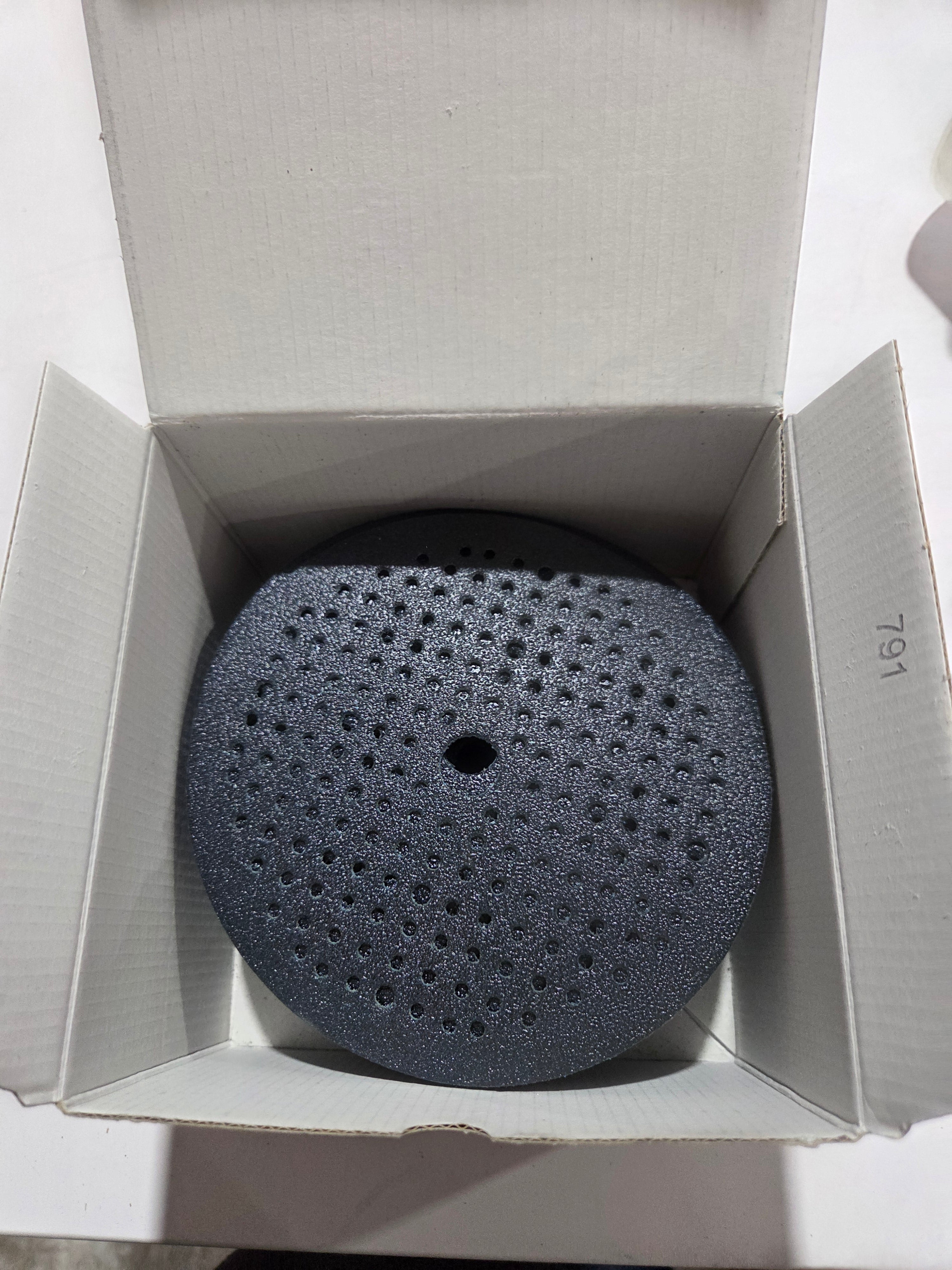 Black perforated round object in an open cardboard box