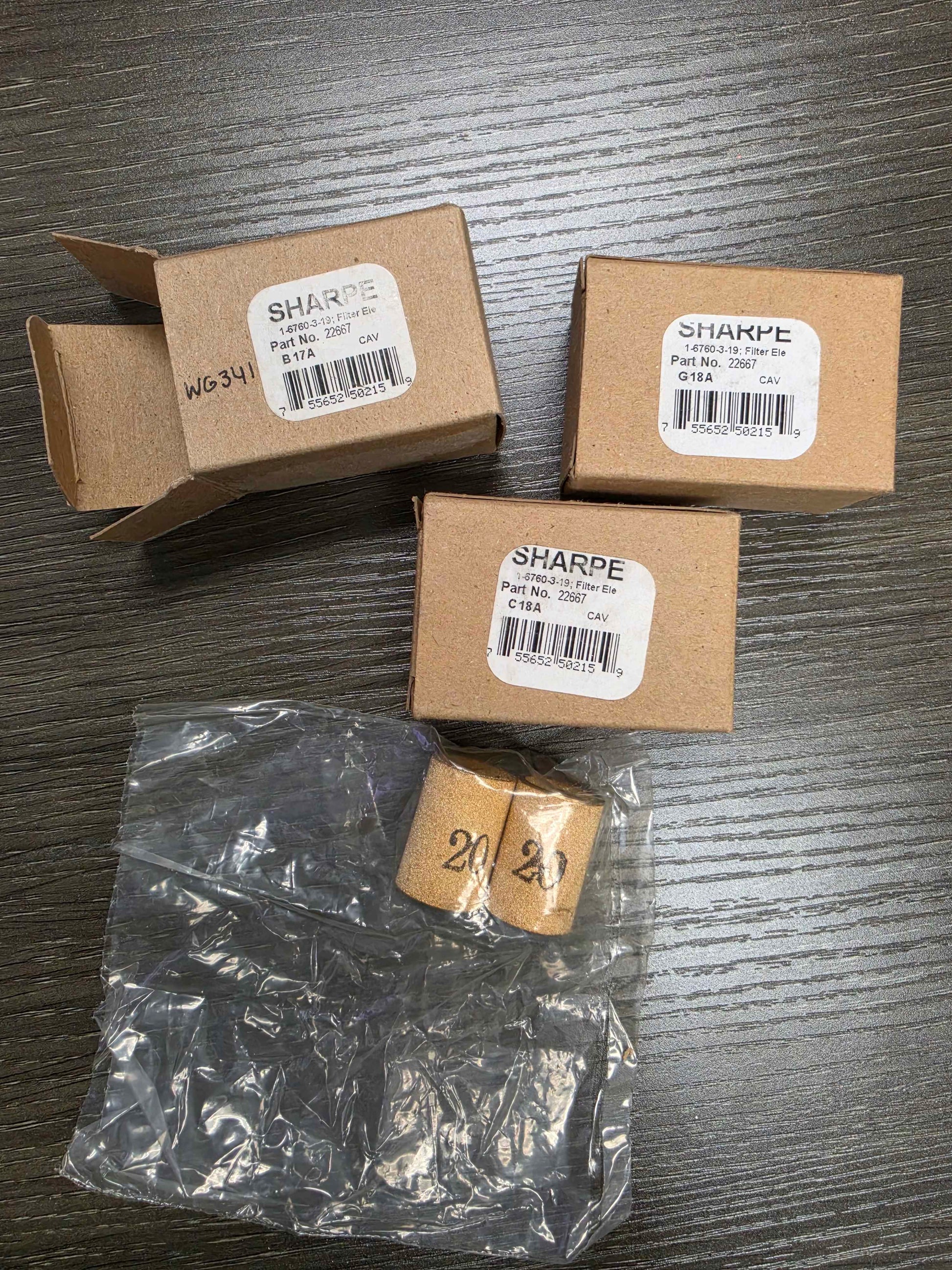 Three cardboard boxes with 'SHARPE' labels and a clear plastic bag with small items on a wooden surface.