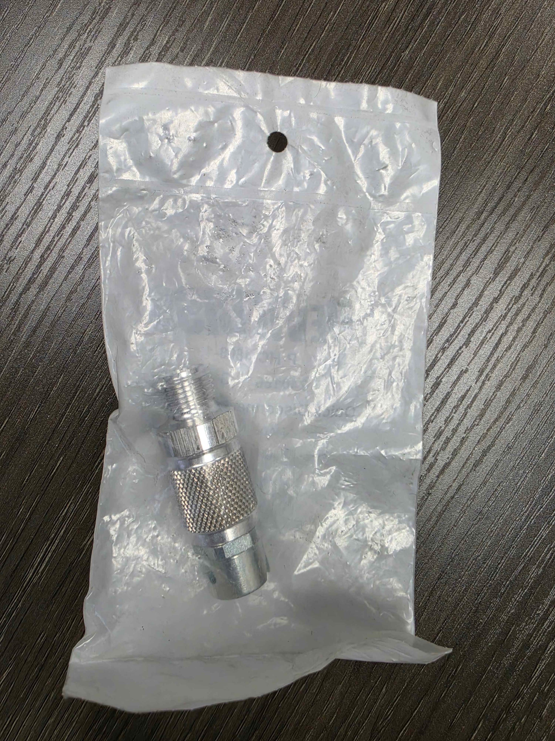 Metal fitting on a clear plastic bag against a dark wooden surface