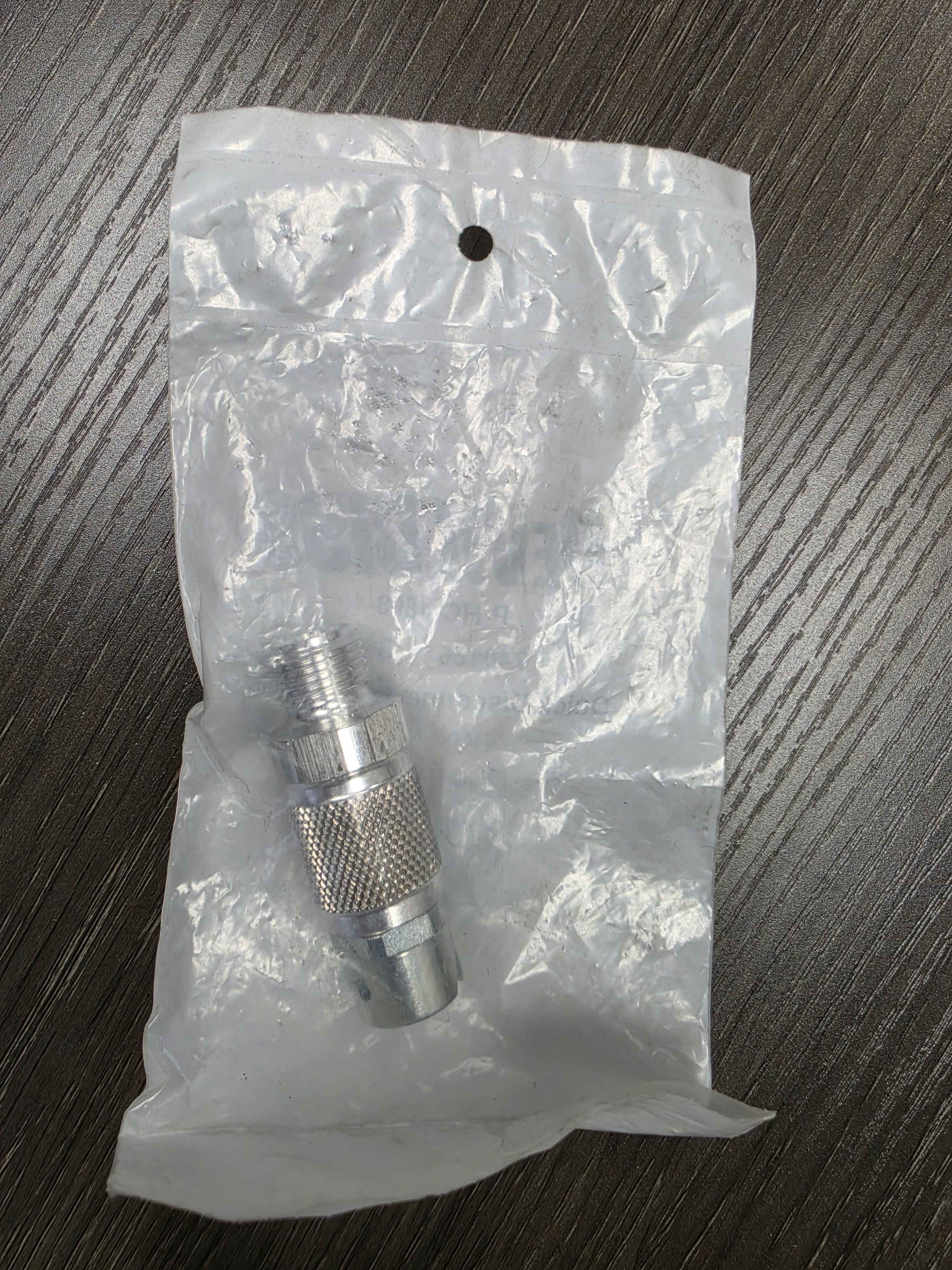 Metal fitting on a clear plastic bag against a dark wooden surface