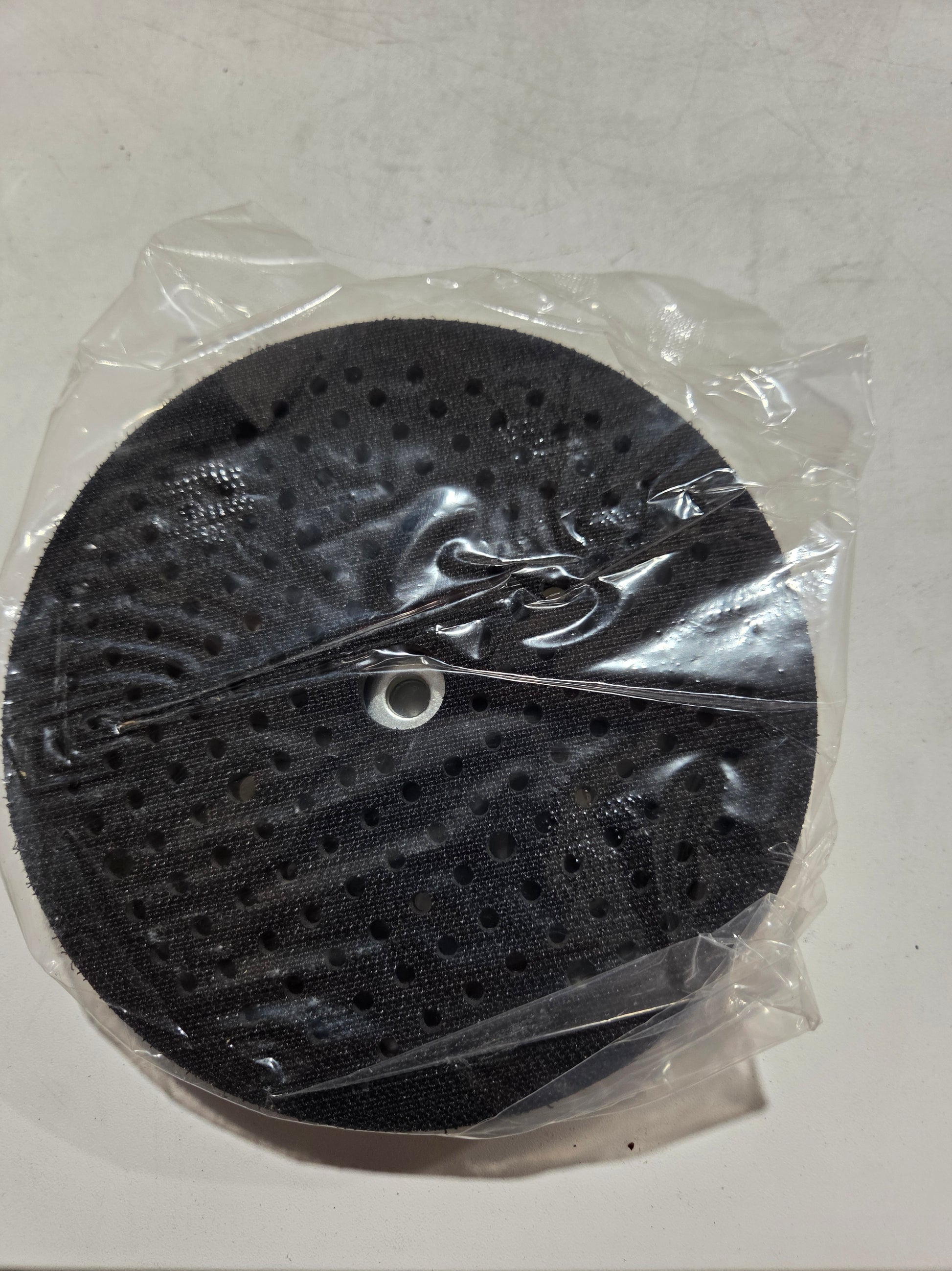 Black circular object with holes in clear plastic packaging on a white background