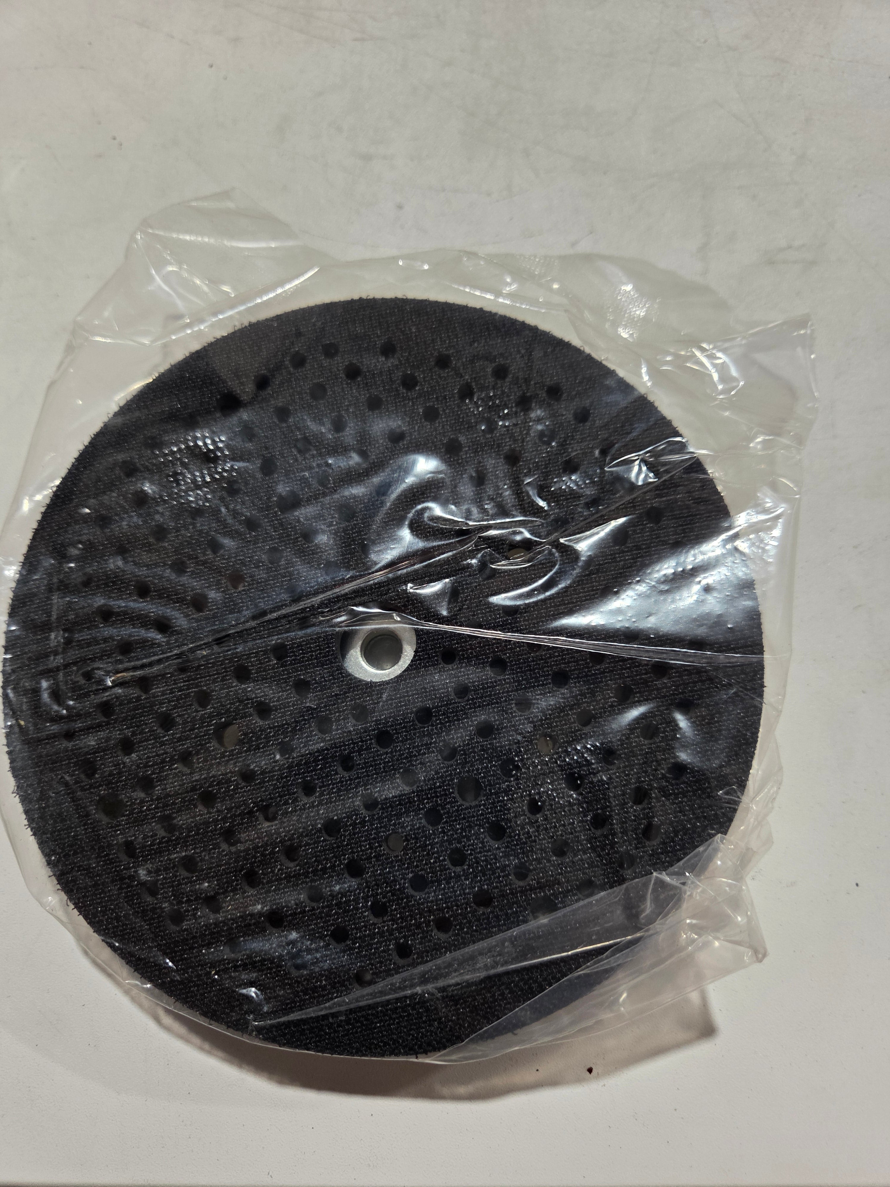 Black circular object with holes in clear plastic packaging on a white background