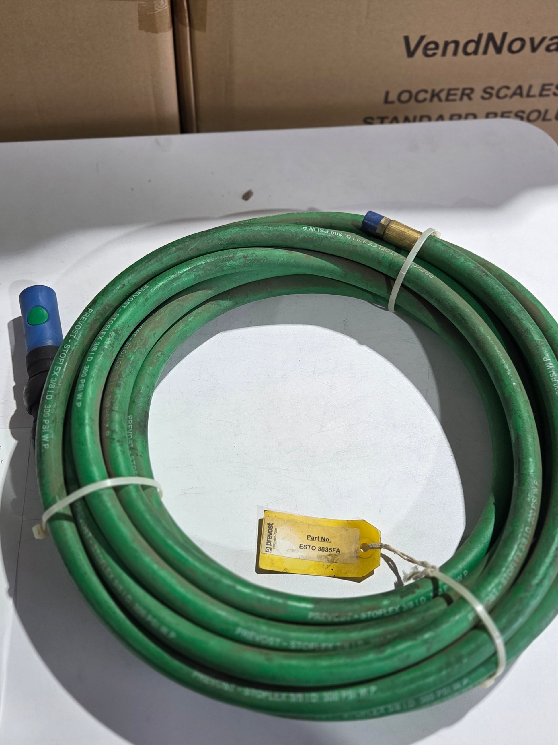Coiled green garden hose with a tag on a white surface