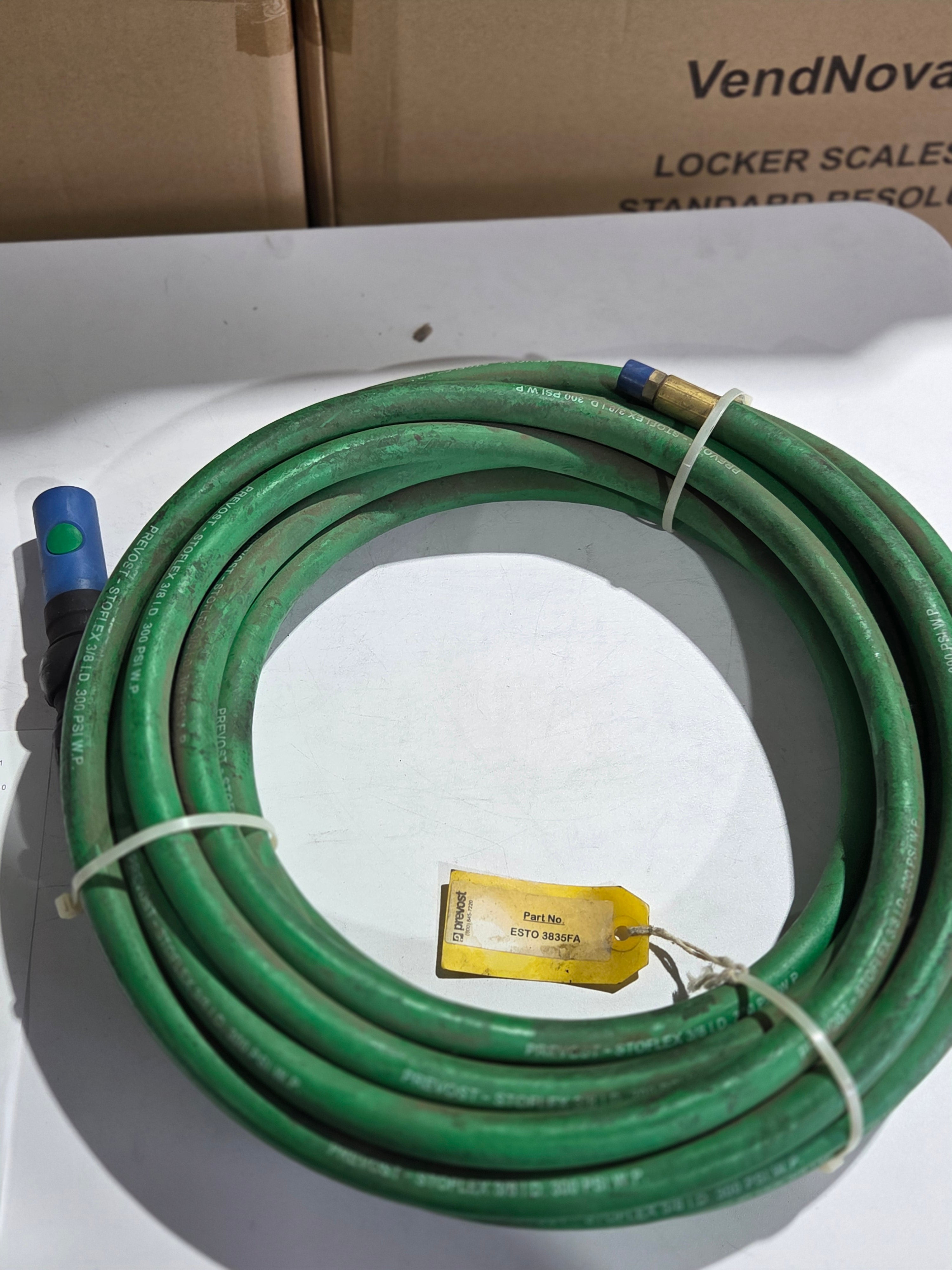 Coiled green garden hose with a tag on a white surface