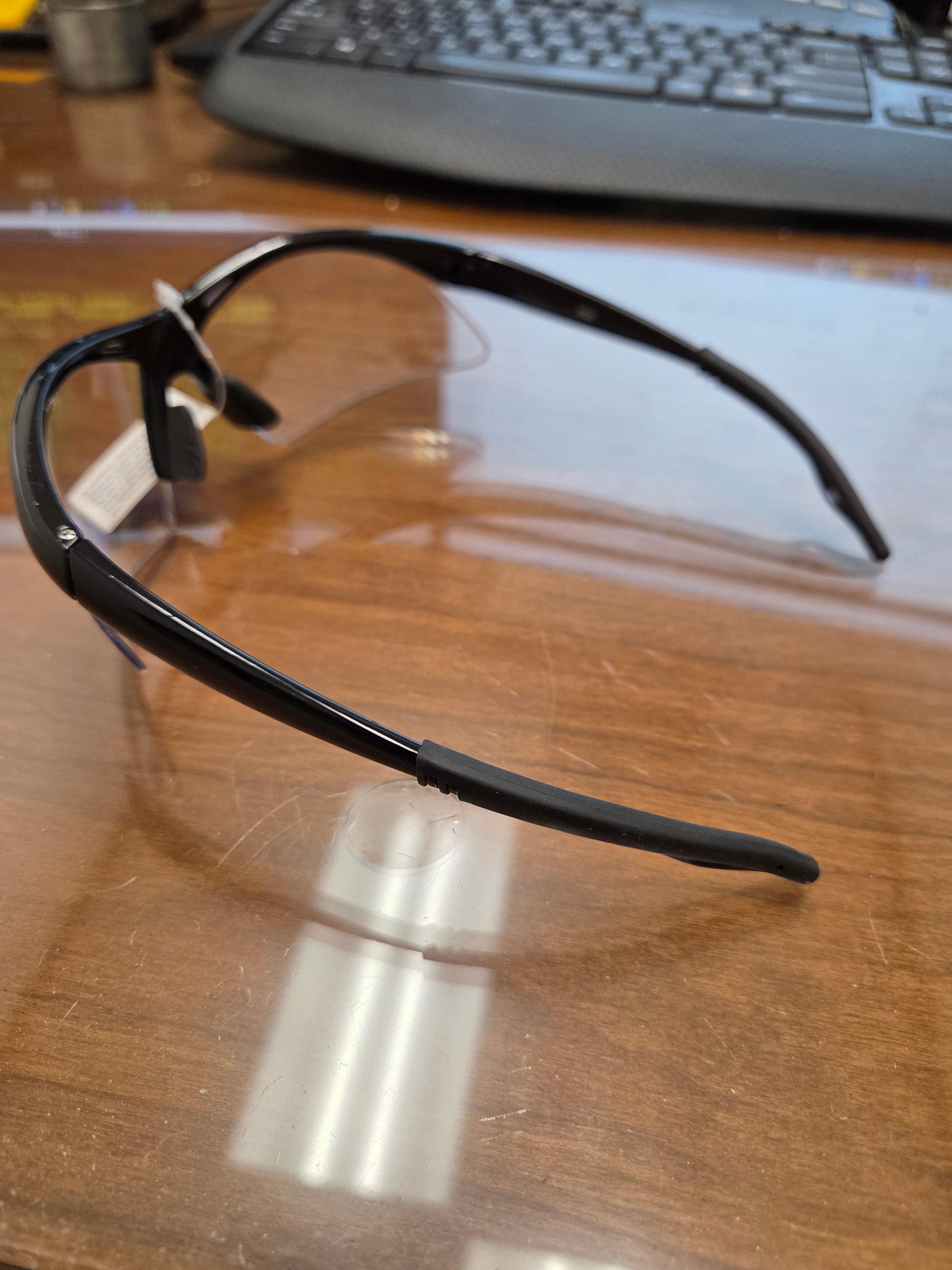 Black safety glasses on a reflective wooden surface with a keyboard in the background