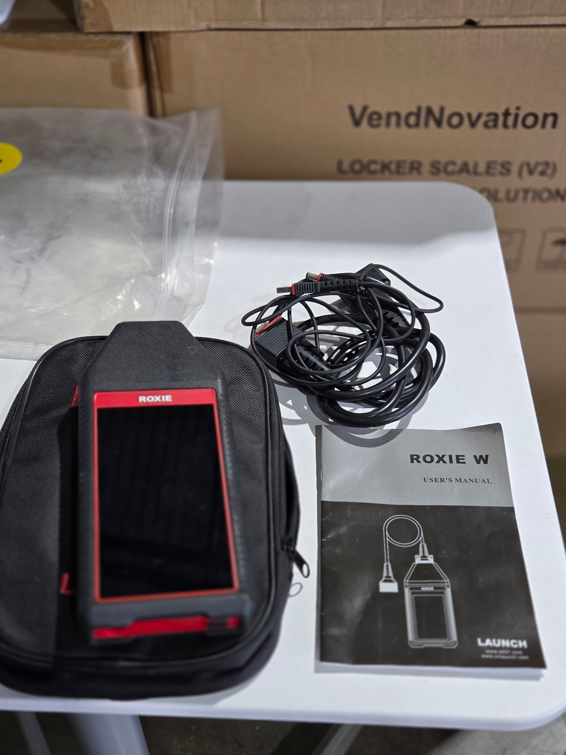 Black and red device with cables and packaging on a white surface