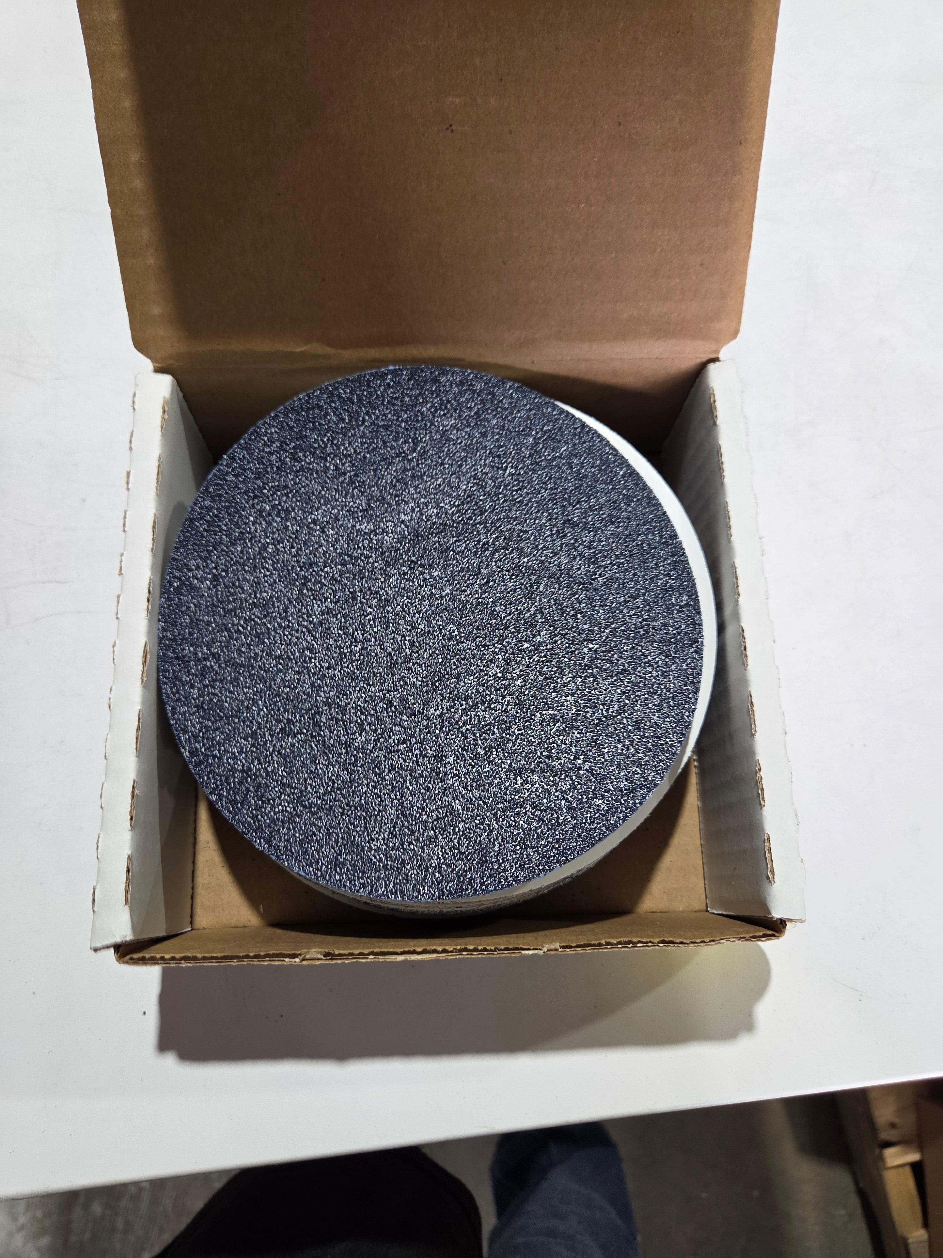 Round gray object in a cardboard box on a white surface