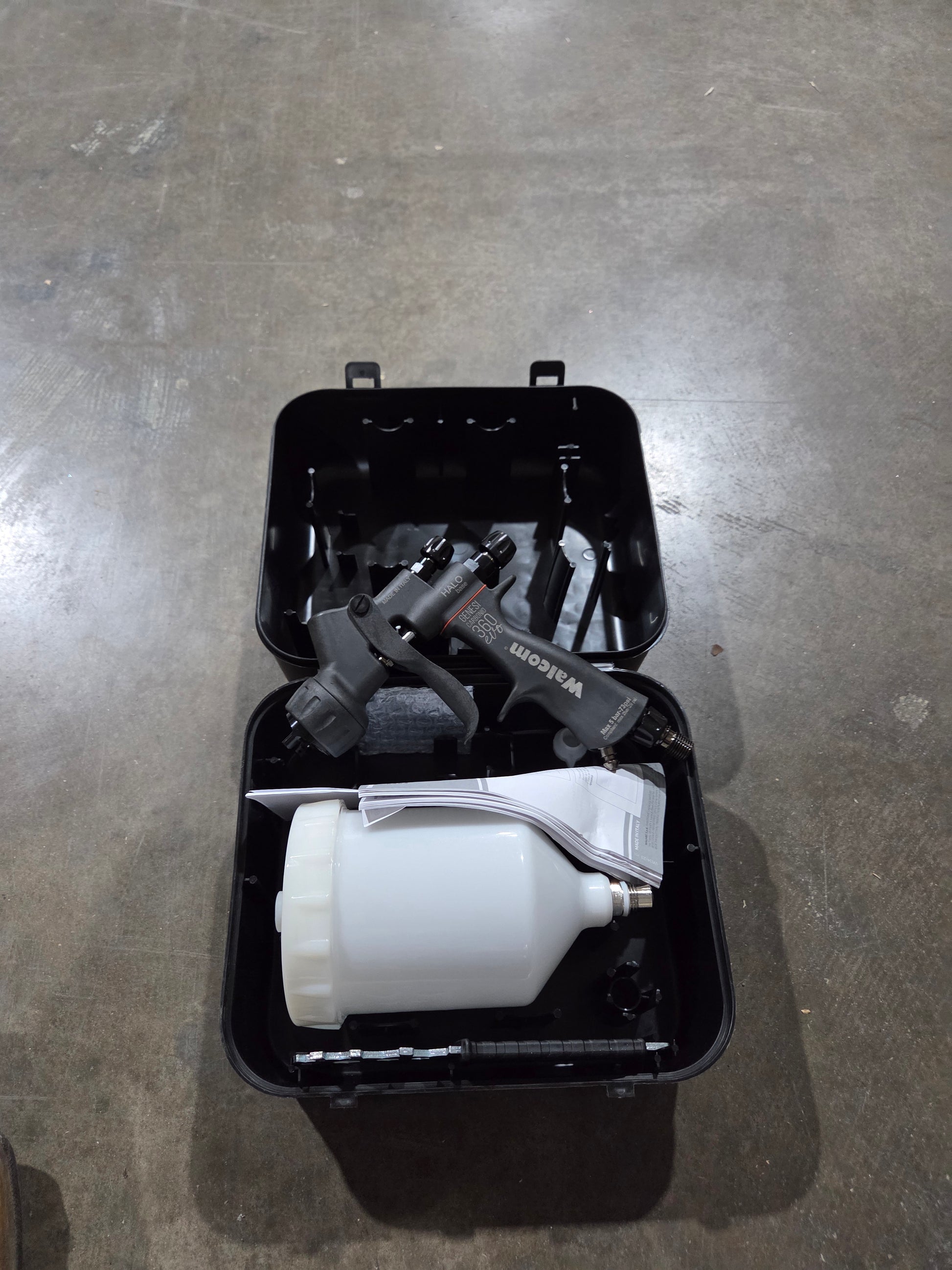 Black toolbox with tools and a white container on a gray floor
