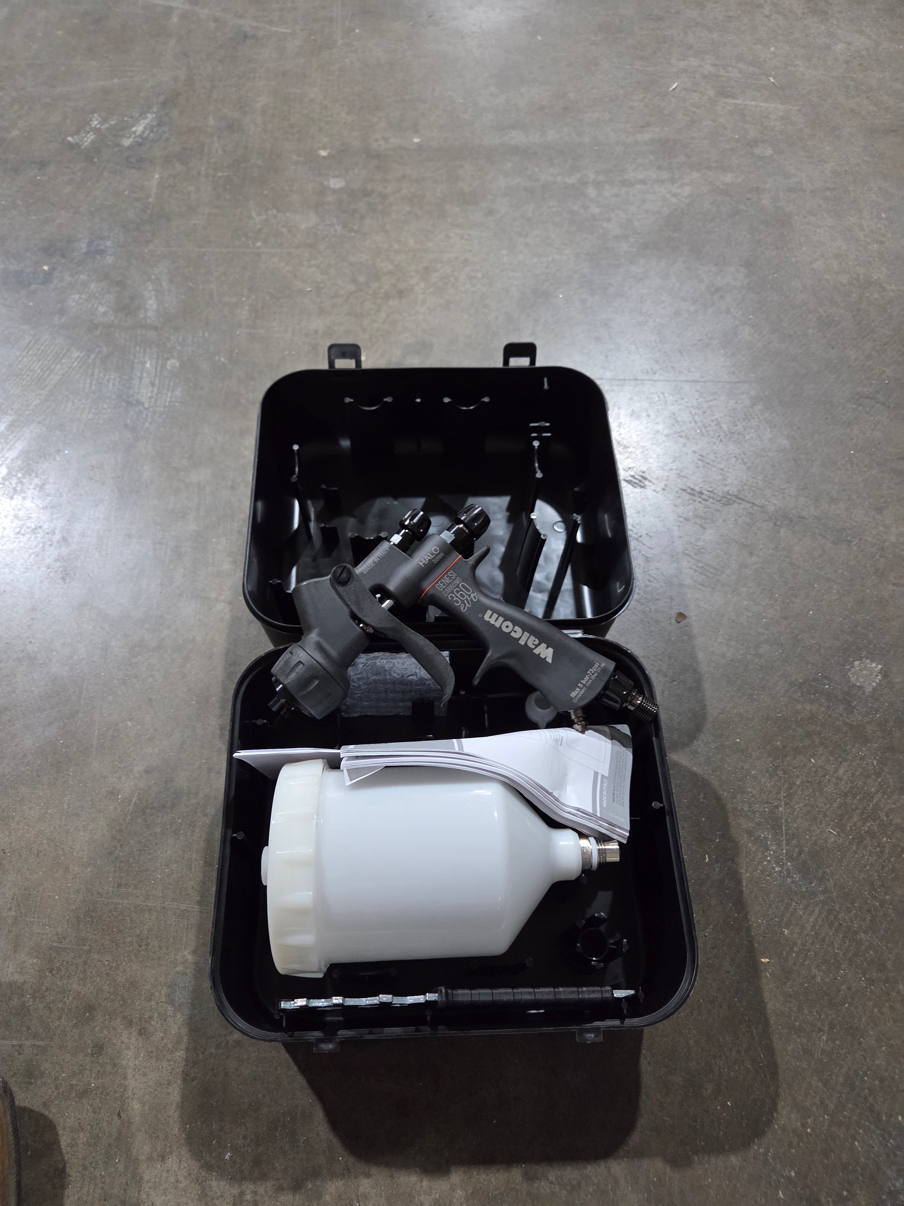 Black toolbox with tools and a white container on a gray floor